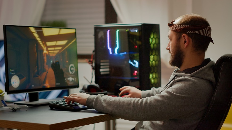Homem jogando game de FPS em PC gamer com gabinete e teclado à mostra — Foto: Reprodução/Unsplash (DC Studio)